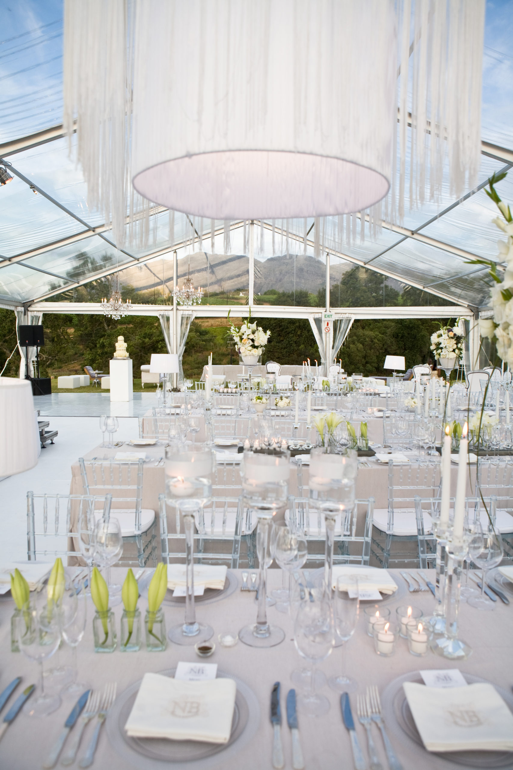 White wedding reception tables inside a glass marquee overlooking the mountains