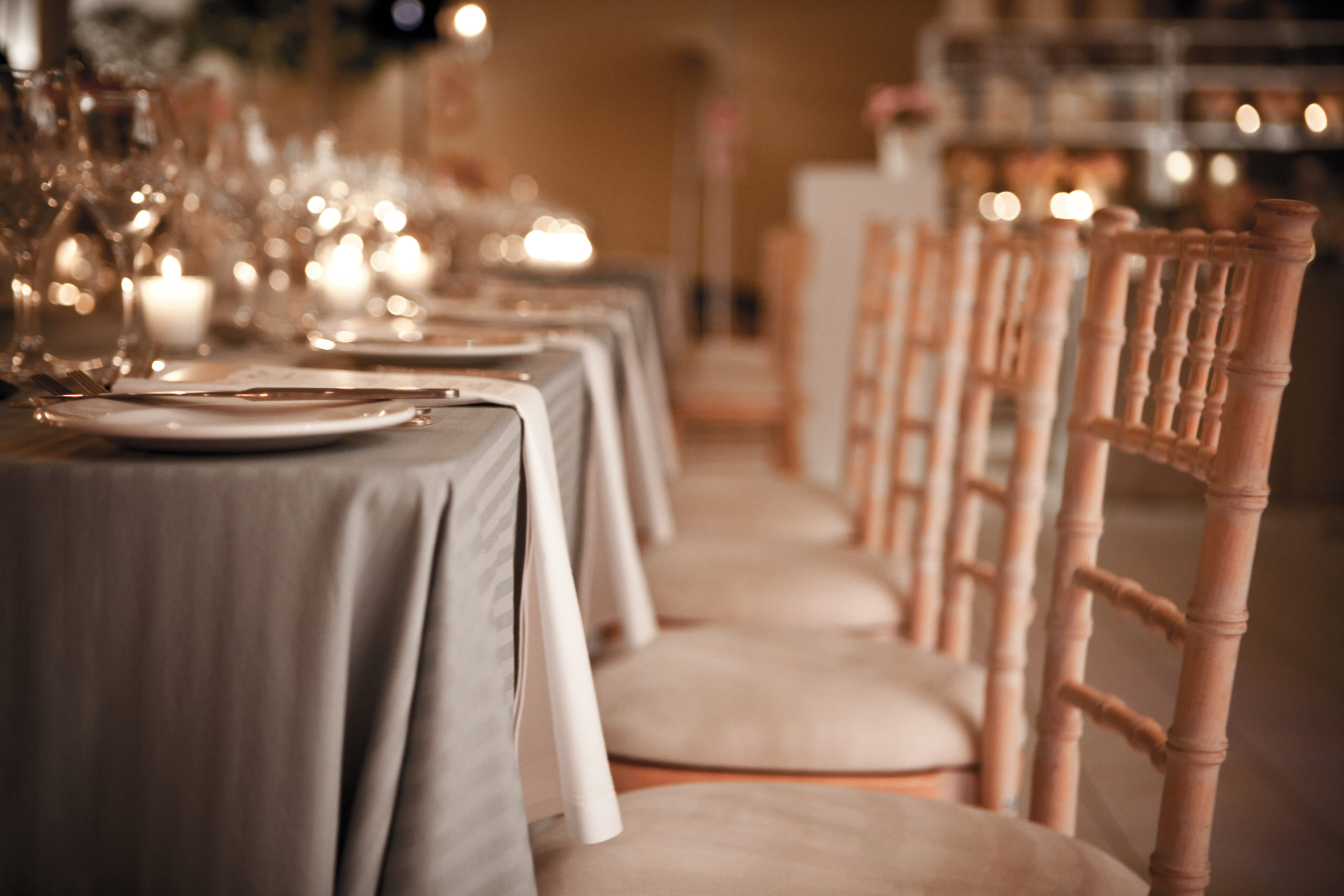 Elegant candlelit event table with white linen, glassware and wooden chairs